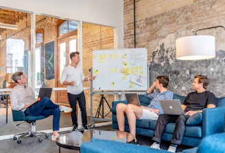 three men sitting while using laptops and watching man beside whiteboard